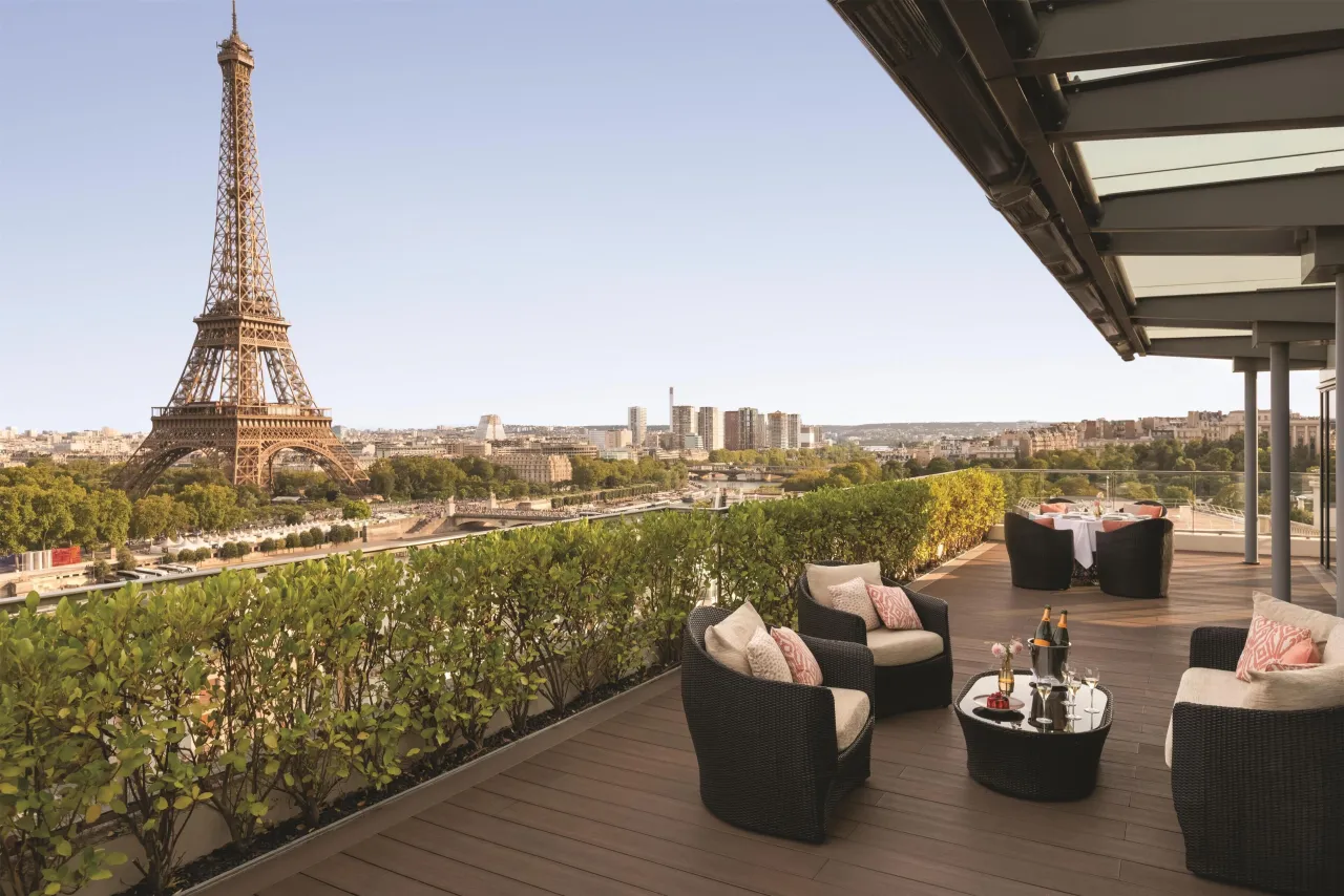 A furnished terrace at Shangri-La Paris facing the Eiffel Tower across the Seine, with armchairs and a hedge