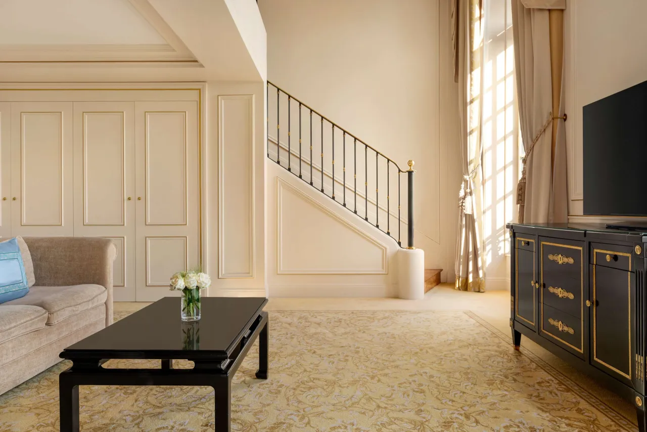 A suite on two levels with a staircase, a sofa, a black lacquered table and tall windows