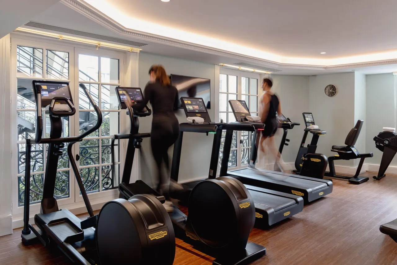 The fitness room with treadmills, elliptical trainers and bicycles beside tall windows