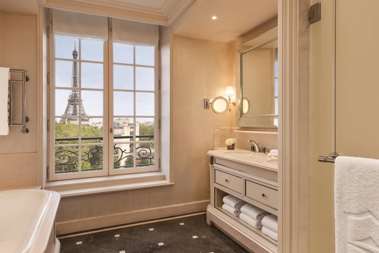 A marble bathroom with a bathtub, its window framing the Eiffel Tower