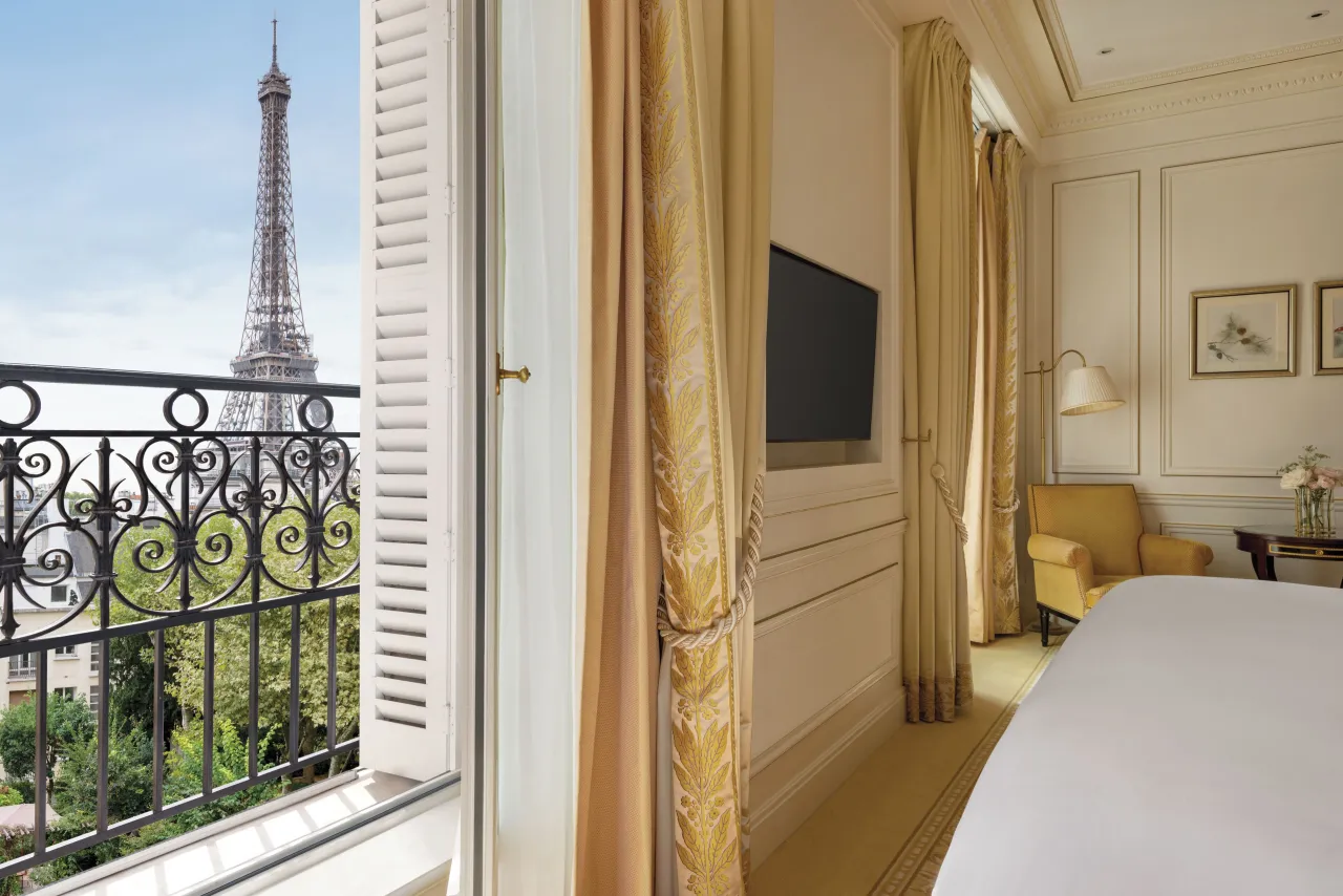 A bedroom with an open French window and a wrought-iron balcony looking onto the Eiffel Tower