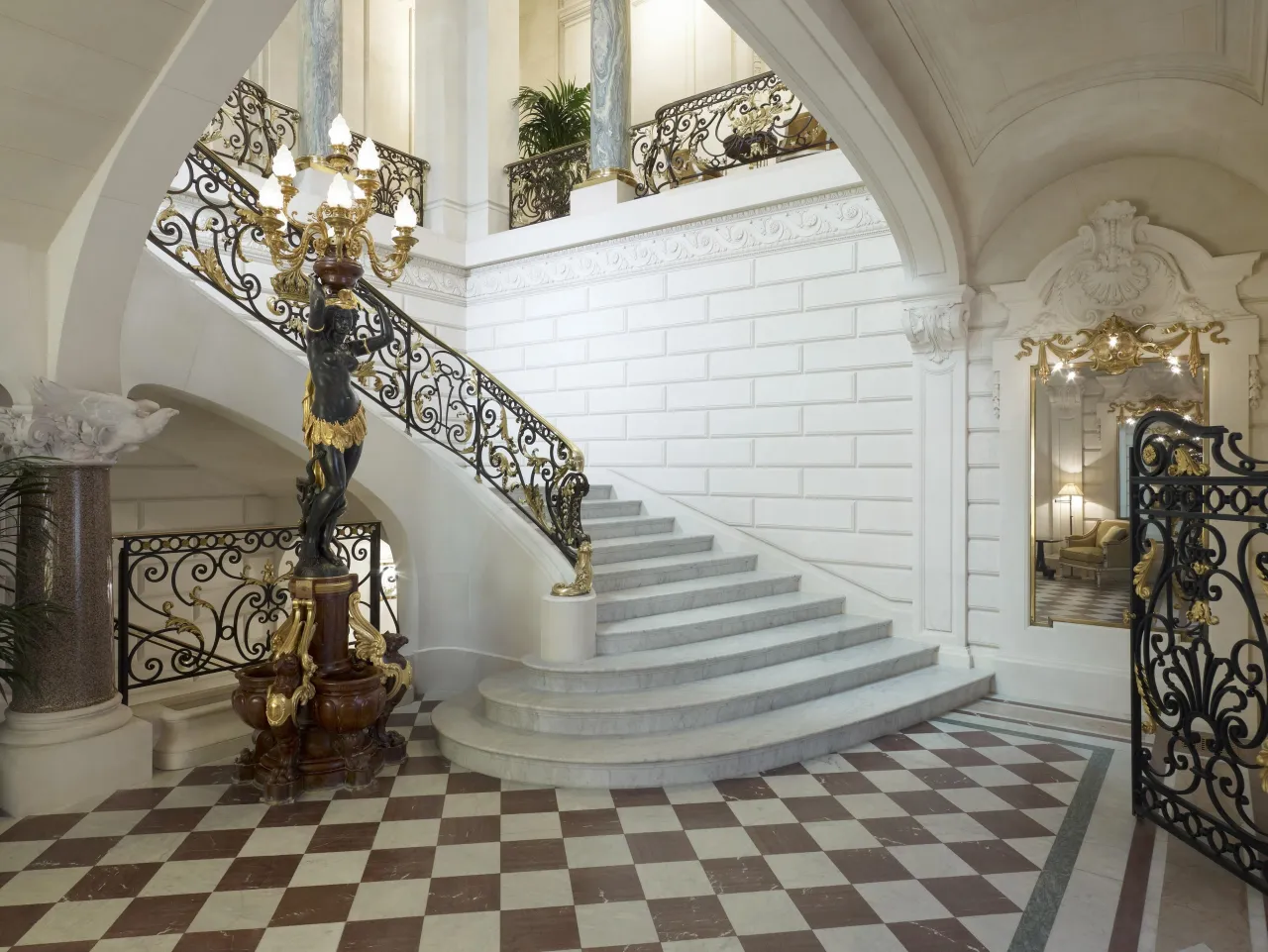 A white stone staircase with a wrought-iron banister and a checkerboard marble floor