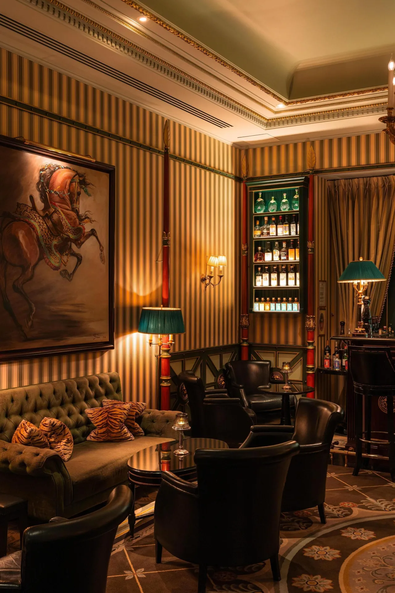 A bar with striped walls, leather armchairs, green lamps and a painting of a horseman
