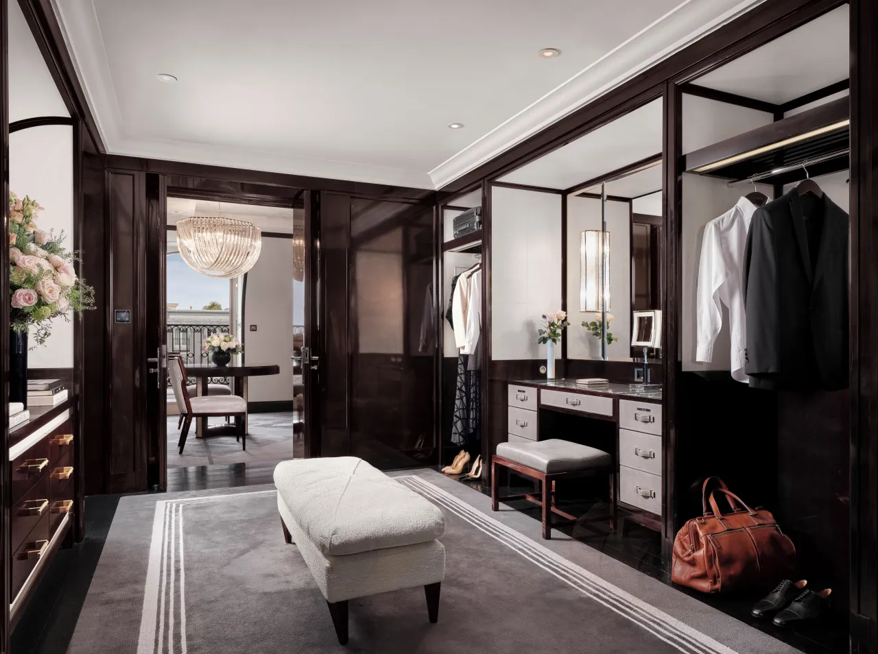 Un dressing aux armoires de bois sombre, coiffeuse, banquette crème et sac de cuir