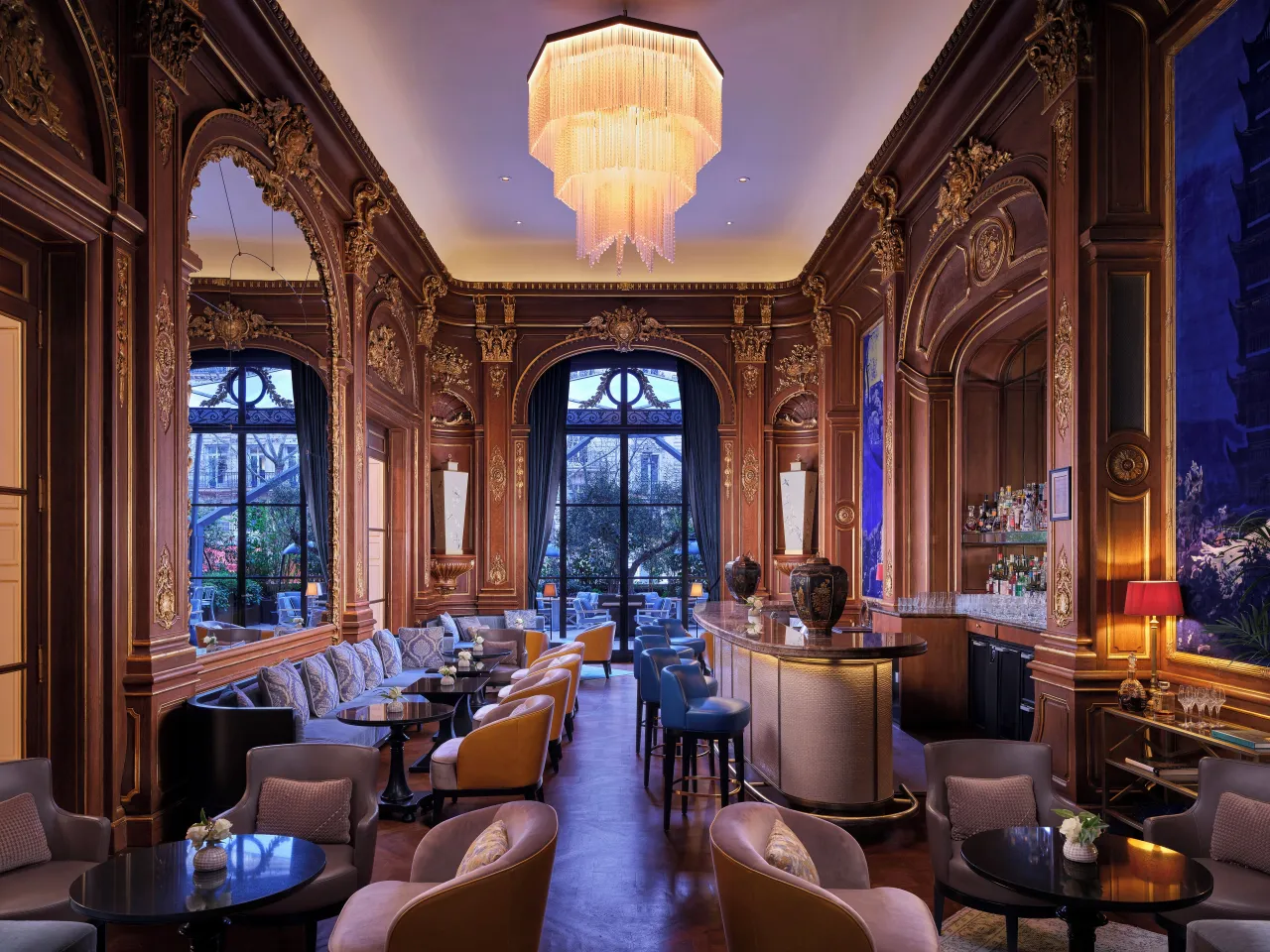 Un bar aux boiseries de chêne sculptées, hauts miroirs, lustre de verre et fauteuils de cuir