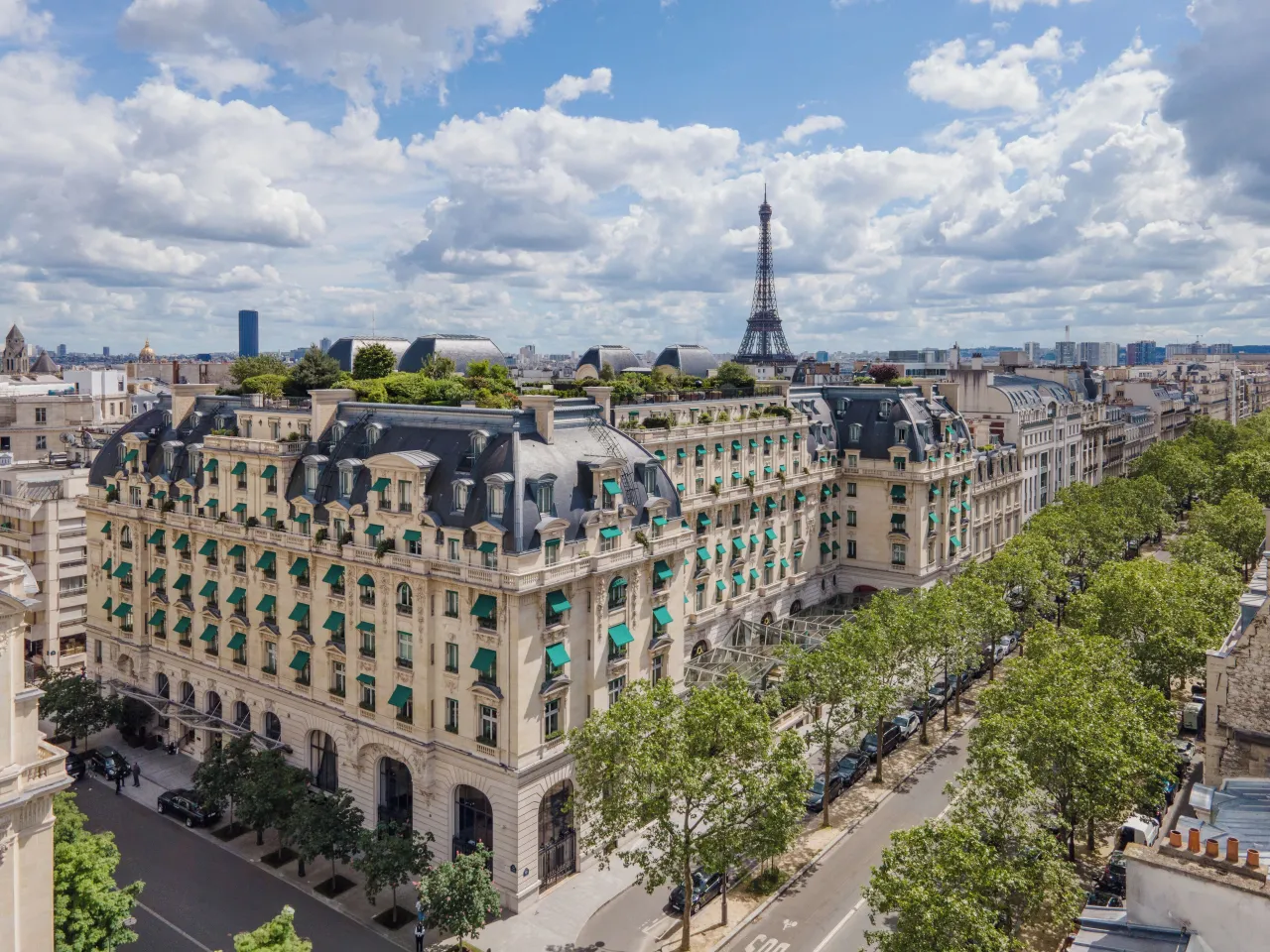 L’hôtel vu d’en haut, à l’angle d’une avenue bordée d’arbres, ses jardins sur le toit et la tour Eiffel au loin
