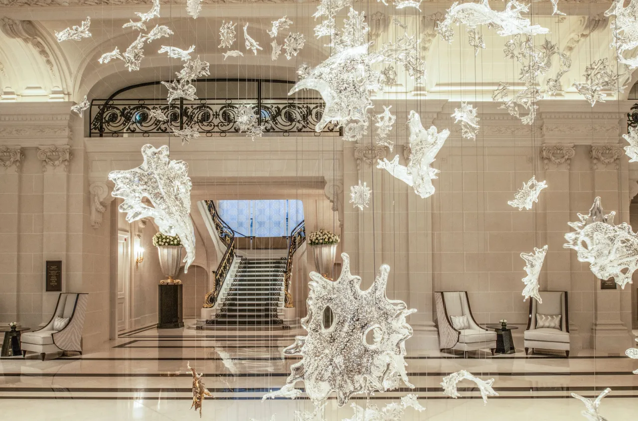 Un hall de pierre claire, un escalier au fond, sous des centaines de feuilles de verre suspendues